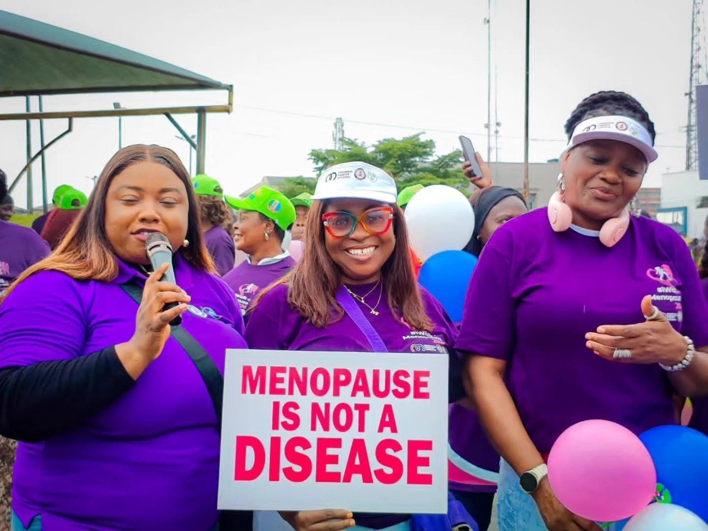 Three women in purple MSI shirts holding a "Menopause is not a disease" placard